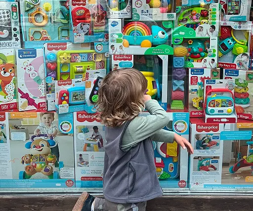 Copil mic privind jucării colorate, educative și pentru bebeluși expuse într-o vitrină de magazin